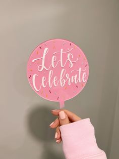 a person holding up a pink sign that says let's celebrate with sprinkles