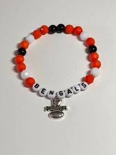 "This is a handmade bracelet representing the Cincinnati Bengals.  Very pretty orange, black, and white beads and a football charm  on a stretchy elastic. Would fit a 7\" wrist easily.     The combination of the colors of the beads, give this bracelet a fun and sporty flair.  Show your support for the Cincinnati Bengals with this stunning beaded bracelet! The  multicolor beads are beautifully accented with a silver tone charm that dangles elegantly from the wrist. Measuring 7 inches in length, t Personalized White Bracelets For Football Season, White Beaded Bracelets For Football Season, Black Team Spirit Adjustable Beaded Bracelets, Adjustable Black Team Spirit Jewelry, Black Adjustable Beaded Bracelets Team Spirit Style, Black Sports Jewelry With Round Beads, Personalized White Beaded Bracelets For Football Season, Black Adjustable Beaded Bracelets For Team Spirit, White Sporty Stretch Bracelet With Round Beads