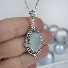 Indulge in the serene beauty of aqua blue chalcedony with this handcrafted filigree art pendant necklace. A stunning 13x18mm faceted oval cut gemstone takes center stage in this exquisite piece, delicately set in silver. The pendant's height of 1.90 inches and width of 1.05 inches make it the perfect statement piece for any outfit. The silver chain measures 20 inches in length, making it the ideal length to rest just below the collarbone. This pendant necklace is the perfect gift option for spec Elegant Oval Aquamarine Necklaces, Elegant Aquamarine Necklace, Elegant Oval Aquamarine Necklace, Elegant Aquamarine Round Pendant Jewelry, Elegant Turquoise Oval Pendant Jewelry, Elegant Chalcedony Jewelry Gift, Oval Aquamarine Gemstone Necklace, Elegant Aquamarine Faceted Necklace, Chalcedony Oval Pendant Necklace For Gift