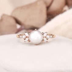 a pearl and diamond ring sitting on top of a white pillow in front of a teddy bear