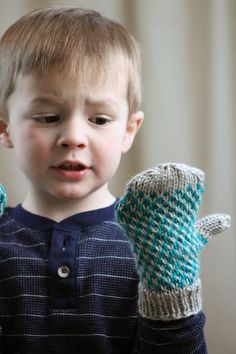 a young boy holding two knitted mittens in his hands