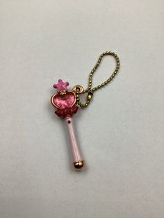 a key chain with a pink heart shaped object hanging from it's side on a white surface