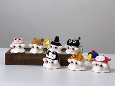 small crocheted snowmen sitting on top of a wooden block, all wearing hats and scarves