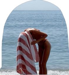 a woman is standing on the beach with an american flag towel in her hand and looking at the water