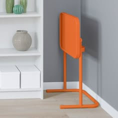 an orange chair sitting in front of a white book shelf with vases on it