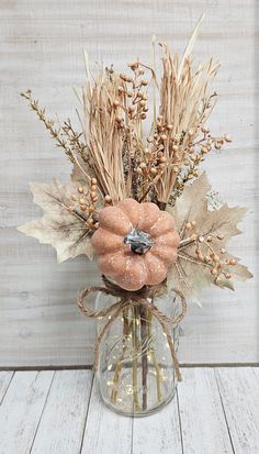 a vase filled with dried flowers and leaves on top of a white wooden table next to a wall