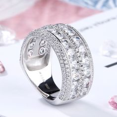 Celebrate your everlasting love story with this elegant band. Stunning as a wedding or anniversary band, two rows of sparkling round stones are set across the center of this band and split by a row of smaller round stones - decorates the ring's impressive shank. A double row of smaller round stones grace the top and bottom of the band, completing this exceptional design. This band is a beautiful reminder of your timeless romance.Carat Weight: 6.575 ctStone Size: 3,1,1.2 mmStone Type: Jeulia® Sto Round Cubic Zirconia Diamond Ring With Rhinestones, Wedding Rings In Diamond White With Rhinestones, Diamond White Wedding Rings With Rhinestones, Wedding Rings With Bling And Round Cut, Cubic Zirconia Rings With Rhinestones For Anniversary, Cubic Zirconia Bands With Diamond Accents, Anniversary Rings With Cubic Zirconia And Rhinestones, Wedding Jewelry With Channel Set Wide Band, Silver Half Eternity Diamond Ring For Marriage