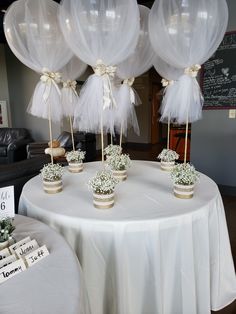 some white balloons sitting on top of a table with flowers and greenery in them