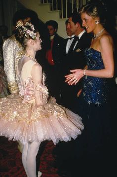 two ballerinas are talking to one another in front of other people wearing tuxedos