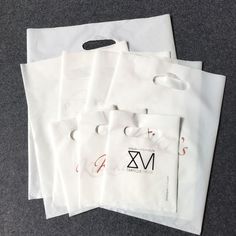 five white shopping bags sitting on top of a gray floor next to each other with the letter m in them