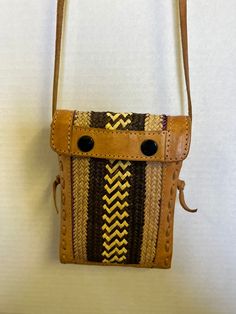 This is a beautiful handcrafted bag made by Tanzanian craftsman. It is made of  light brown natural leather with front and back panels of woven plant fibers similar to wicker. The fibers are a light natural colored wicker strips  with darker strips and a zig zag pattern in the center.  The body of the purse measures 7.25 inches tall by 5.25 inches wide. The leather strap measures 18 inches long. It works well as a cell phone bag. It is sturdy without tears or breaks.  The lining  of the bag is a sturdy soft canvas like material and it closes with two large snaps. There is a little discoloration of the leather about 1.5 inches long on the back. ( see the last photo) It is stamped with the logo of Tasmanian Craftsmen. Cell Phone Bag, Handcrafted Bags, Plant Fibres, Leather Weaving, Zig Zag Pattern, Phone Bag, Handmade Leather, Hand Bag, Natural Leather