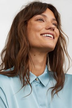 a close up of a person wearing a blue shirt and looking to the side with a smile on her face