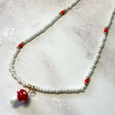 This Beaded White Necklace Has A Red Mushroom Charm Circle Charm Necklace, Perfume Locket, White Beaded Necklaces, Red Mushroom, Locket Pendant Necklace, Elephant Necklace, Stone Beaded Necklace, Long Chain Necklace, Teardrop Necklace