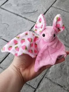 a hand holding a pink stuffed animal with strawberry print on it's wings and ears