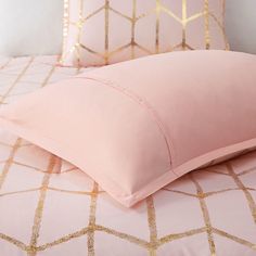 two pink pillows on top of a bed with gold foiled sheets and pillow cases