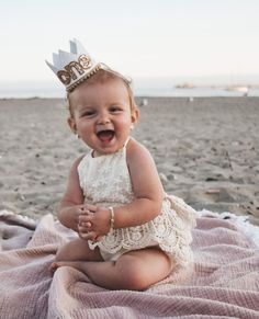 a baby sitting on the beach wearing a tiara