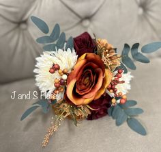 a bridal bouquet on a couch with leaves and flowers in the center, including an orange rose