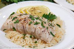 a white plate topped with fish and rice next to lemon wedges on a table