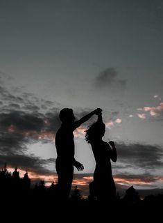 a man and woman are silhouetted against the evening sky with their arms in the air