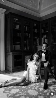 a man sitting next to a woman on the floor in front of a bookcase