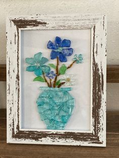 a blue vase with flowers in it sitting on a wooden shelf next to a white frame