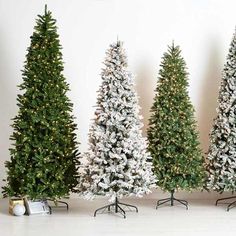 three artificial christmas trees are lined up against a white wall