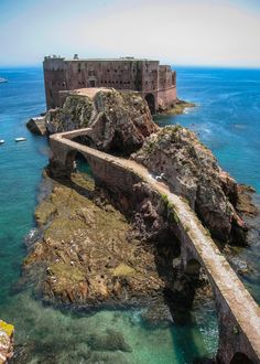 an old castle is on the edge of a cliff over looking the water and rocks