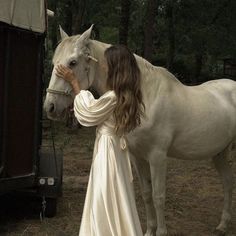 a woman in a white dress standing next to a horse and looking at it's face