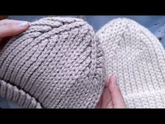 someone is holding two knitted beanies in their hands, one white and the other light gray