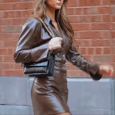 a woman in a brown leather dress is carrying a black purse and walking down the street