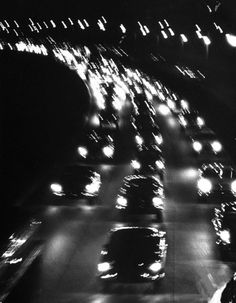 black and white photograph of cars driving down a busy street at night with headlights on