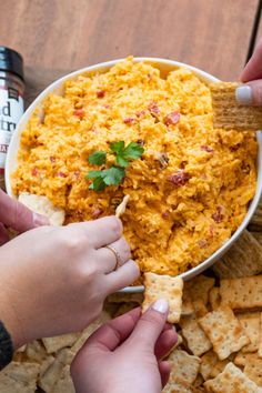 two hands reaching for a cracker over a bowl of cheese and bacon dip surrounded by tortilla chips