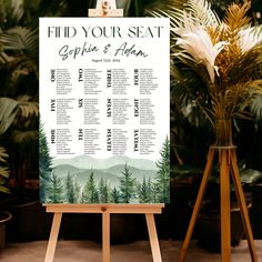 a wedding seating chart on an easel in front of potted plants and greenery