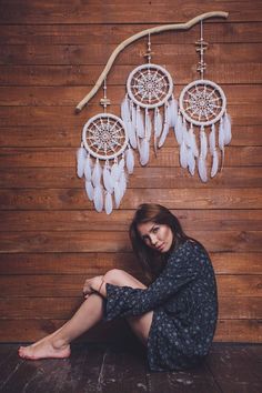 a woman sitting on the floor in front of a wall with dream catchers hanging from it