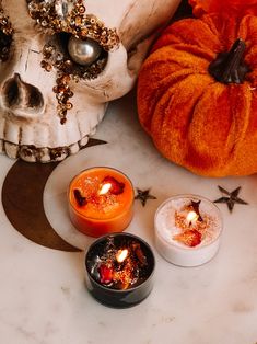 three candles sitting on top of a white table next to a skull and pumpkins