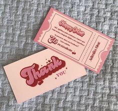 two pink and red thank you cards on top of a gray cloth covered tablecloth