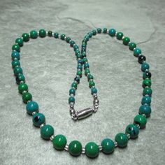 This graduated necklace features unusual Chrysocolla beads. At each end of the necklace are fifteen 4mm Chrysocolla beads, followed by eleven 6mm Chrysocollas and finally in the middle of the necklace eleven 8mm beads. All these Chrysocolla beads are separated by silver lined clear Glass seed beads. All the metal work is Stainless Steel including the magnetic clasp and the earwires on the free matching earrings. Necklace and earring come enclosed within a dark brown fine Velvet bag. Chrysocolla is a greenish/blue mineral of hydrated copper silicate. Is both refreshing and rejuvenating. During the Renaissance it was ground into powder to make pigment for paint. It's soothing properties guides to a state of calm and confidence. It is a stone of communications and of empowerment of the femini Green Chrysocolla Round Bead Necklaces, Green Chrysocolla Single Strand Necklace, Green Chrysocolla Round Beads Necklace, Green Chrysocolla Beaded Necklaces With Round Beads, Green Chrysocolla Beaded Necklaces, Jade Bead Necklace, Graduation Necklace, 8mm Beads, Wire Necklace