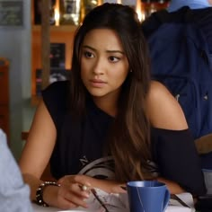 a woman sitting at a table with a blue cup in front of her and another person behind her