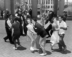 a group of people standing around each other in front of some tall buildings and pillars