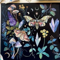 a painting of moths and flowers on a black background with paintbrushes next to it