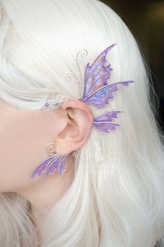 a close up of a person with white hair and butterfly ear clips on their ears