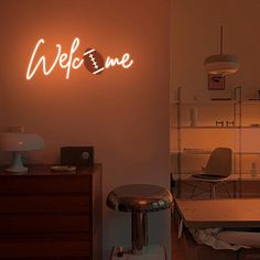 a neon sign that reads welcome in the corner of a room with a desk and chair