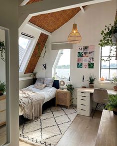 an attic bedroom with a bed, desk and plants in the window sill area