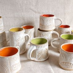 a group of coffee mugs sitting on top of a white cloth covered tablecloth