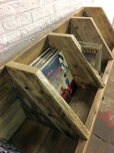 a wooden shelf with magazines in it on top of a floor next to a brick wall