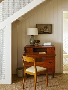 a room with a desk, chair and lamp next to a stair case in the corner