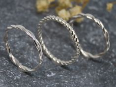 two silver rings sitting next to each other on top of a stone surface with dried flowers in the background