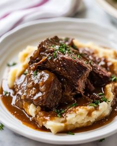 a white plate topped with mashed potatoes and beef on top of gravy