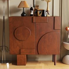 a wooden cabinet sitting on top of a hard wood floor next to a lamp and vase