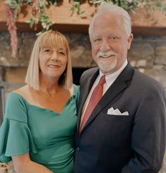 an older man and woman standing next to each other in front of a fire place